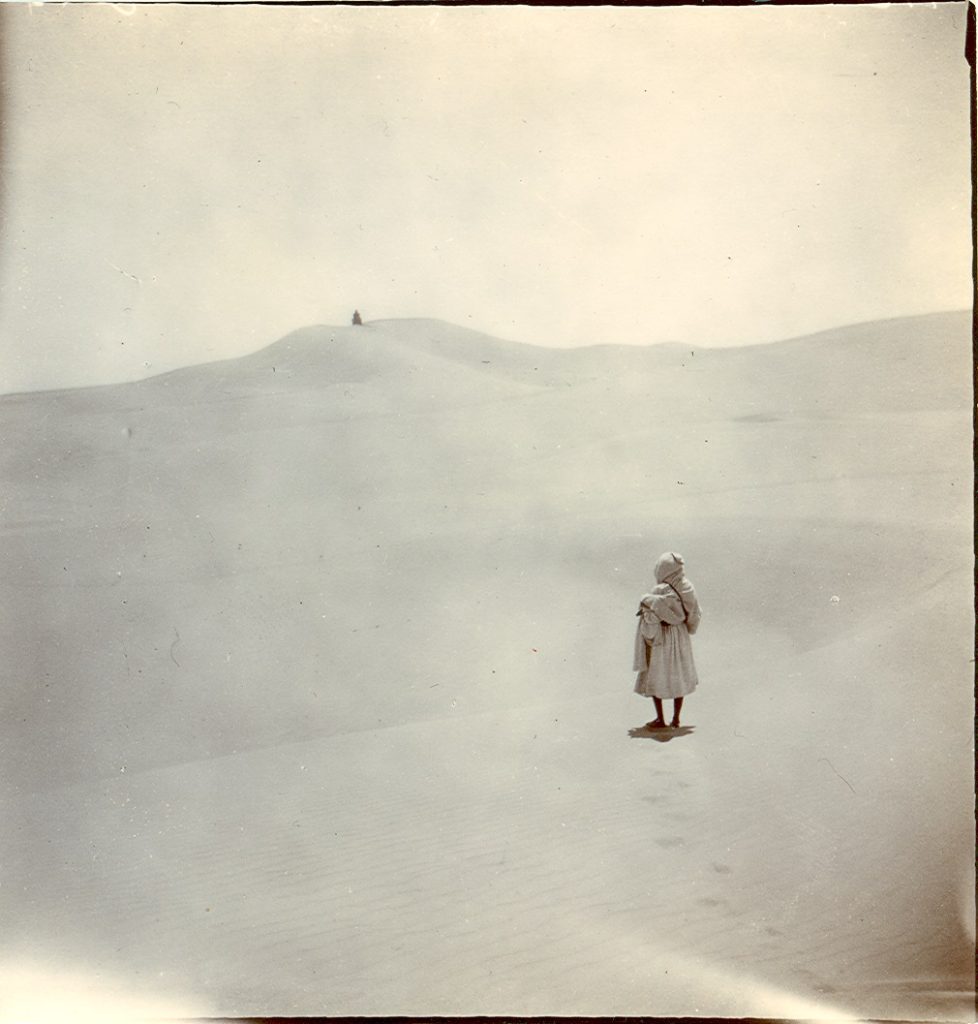Photograph of man standing in desert surrounded by sand dune
